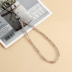 Pink and clear crystal beaded phone charm strap with polished metal ring on beige background