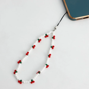 Close-up of white beaded phone strap featuring red cherry charms on a clean background
