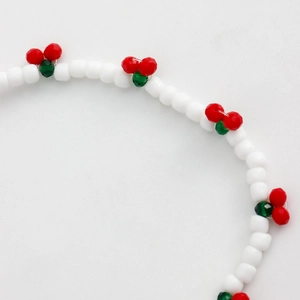 Detail of white beaded phone strap with red cherry charms and multifaceted green beads