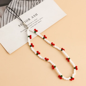 White beaded phone lanyard with red cherry charms and metallic clasp over beige background