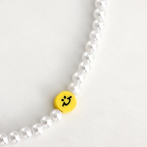 Gros plan d'une dragonne de téléphone avec perles blanches et charm smiley jaune