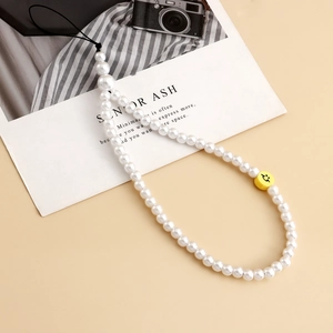 Détail du cordon de téléphone en perles avec une perle smiley jaune sur fond beige