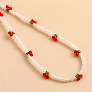 Detailed view of white seed bead phone strap featuring cute red cherry accents