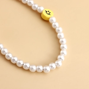Détail de la dragonne de téléphone en perles avec une perle souriante jaune au centre
