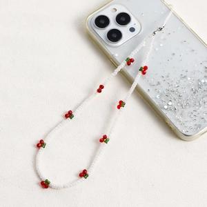 Detail of beaded phone lanyard with white pearls and red cherry charms on sand texture