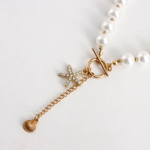 Detail of gold starfish pendant with rhinestones and shell on white pearl necklace