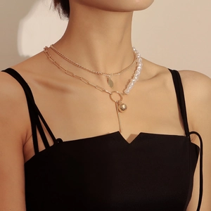 Collana dorata a due strati con perle bianche e pendenti geometrici su modella