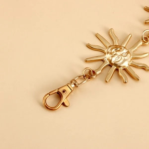 Close-up of golden metal sun charm with smiley face and lobster clasp on waist chain