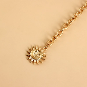 Detailed close-up of a golden metal waist chain with sun and moon face relief pendant