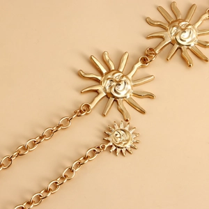 Detail of golden metal waist chain featuring three smiling sun charms on a ring link belt