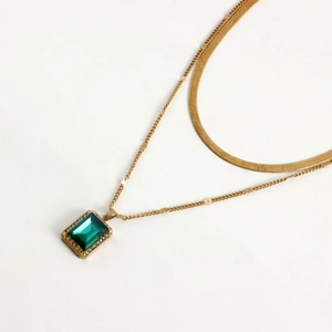 Detail of double-layer gold snake chain featuring a rectangular emerald gemstone pendant