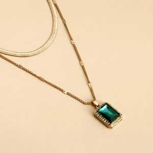 Detail of double-layer necklace with snake chain and emerald-colored gemstone pendant