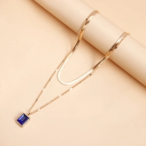 Detail view of double-layer gold snake chain necklace with rectangular blue gemstone pendant