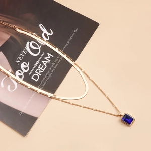 Detail of double-layer gold necklace featuring flat snake chain and blue gemstone pendant
