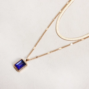 Detailed macro view of layered gold snake chain with a rectangular blue gemstone pendant