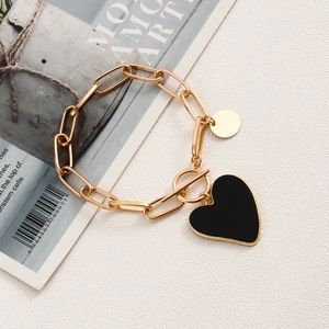 Detailansicht eines goldfarbenen Gliederkettenarmbands mit schwarzem Herzanhänger und Knebel