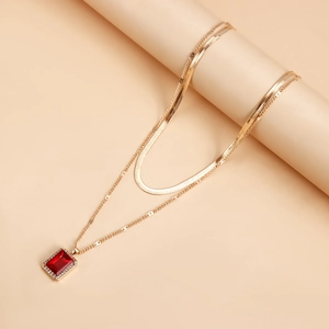 Detail of a double-layered gold snake chain necklace with a red rectangular pendant