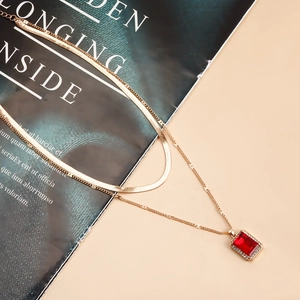 Close-up of double-layered gold snake chain featuring a red gemstone pendant with zircons