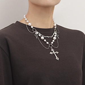 Double-layered necklace with bright white pearls, stars, and cross pendant on model.