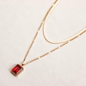 Detail of double-layer gold snake chain featuring a red gemstone rectangular pendant