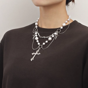 Double-layered pearl necklace with cross pendant and star charm on dark knitwear