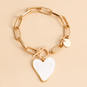 Detailansicht eines goldfarbenen Kettenarmbands mit weißem Herzanhänger und Knebelverschluss