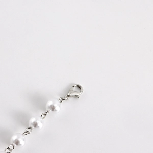 Detail view of a silver lobster clasp and high-gloss pearls on a layered cross necklace