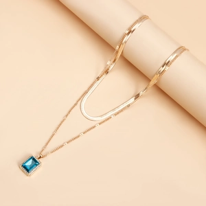 Detail of double-layer gold snake chain featuring a rectangular blue gemstone pendant