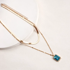 Macro detail of double-layer gold necklace with rectangular blue gemstone pendant