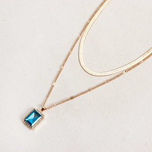 Detail of double-layer gold necklace with rectangular blue gemstone and snake chain