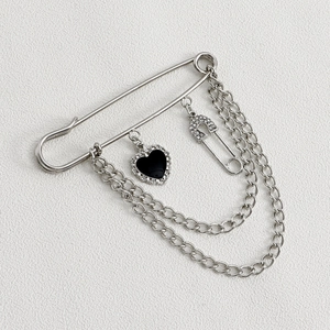 Detalle de broche punk plateado con cadena, colgante de corazón negro y strass brillante