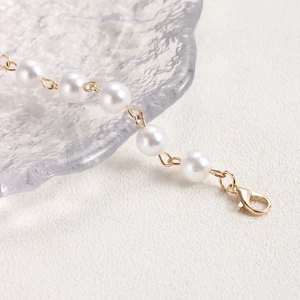 Detailed close-up of white pearls on a gold chain with a secure lobster clasp