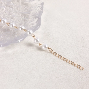 Detail of high-gloss pearl necklace with gold-plated clasp on a white textured background