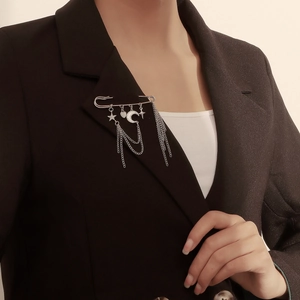 Broche argentée avec breloques étoile et lune et pompons sur revers de veste noire