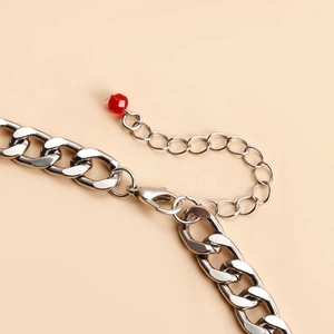 Detail of silver cuban chain necklace with lobster clasp and red bead charm