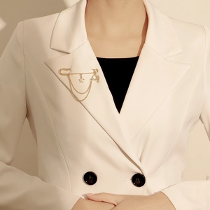 Détail d'une broche étoile et planète dorée avec doubles chaînes sur un blazer clair