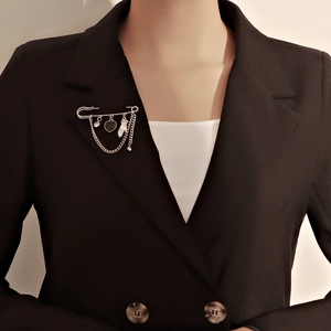 Broche de imperdible plateado con corazón negro y cadenas sobre una chaqueta negra