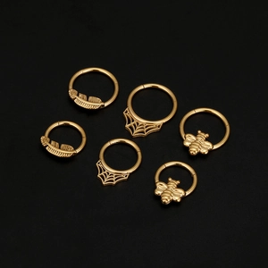 Detalle del set de piercings dorados con diseños de abeja, pluma y telaraña