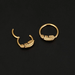 Detalle macro de aros clicker dorados con textura de pluma y mecanismo de cierre