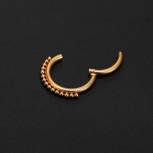 Detail of a 316L gold nose ring with a beaded clicker design on a black background