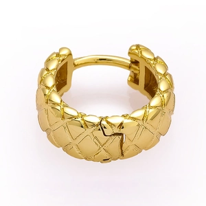 Close-up of golden huggie earring with quilted pattern and high-polish metal texture