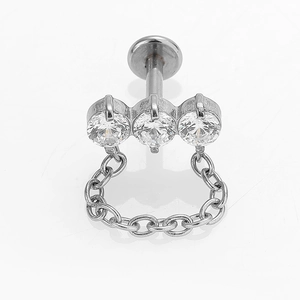 Detalle de un piercing labret de acero 316L con tres circonitas y una cadena colgante