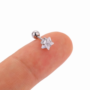Detailed close-up of a tiny star-shaped zircon ear stud held on a fingertip for scale