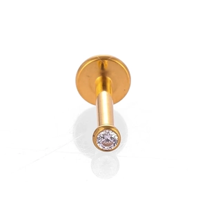 Détail macro du piercing labret en titane doré avec zircone ronde sertie clos