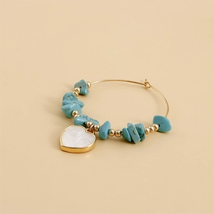 Detail of bohemian gold hoop earring with turquoise beads and a white heart pendant