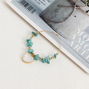 Detail of bohemian gold hoop earrings with turquoise stones and white heart shell pendant