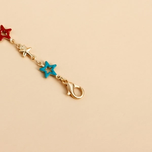 Macro detail of golden body chain featuring colorful star charms and lobster clasp