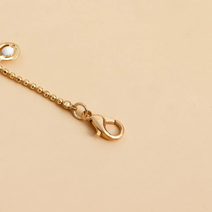 Macro detail of golden metal beaded body chain featuring a secure lobster clasp closure