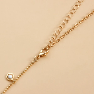 Macro detail of gold lobster clasp, extension chain and white shell inlay round pendant