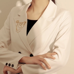 Détail d'une broche à chaînes dorées avec pendentifs cœur et étoile sur blazer blanc